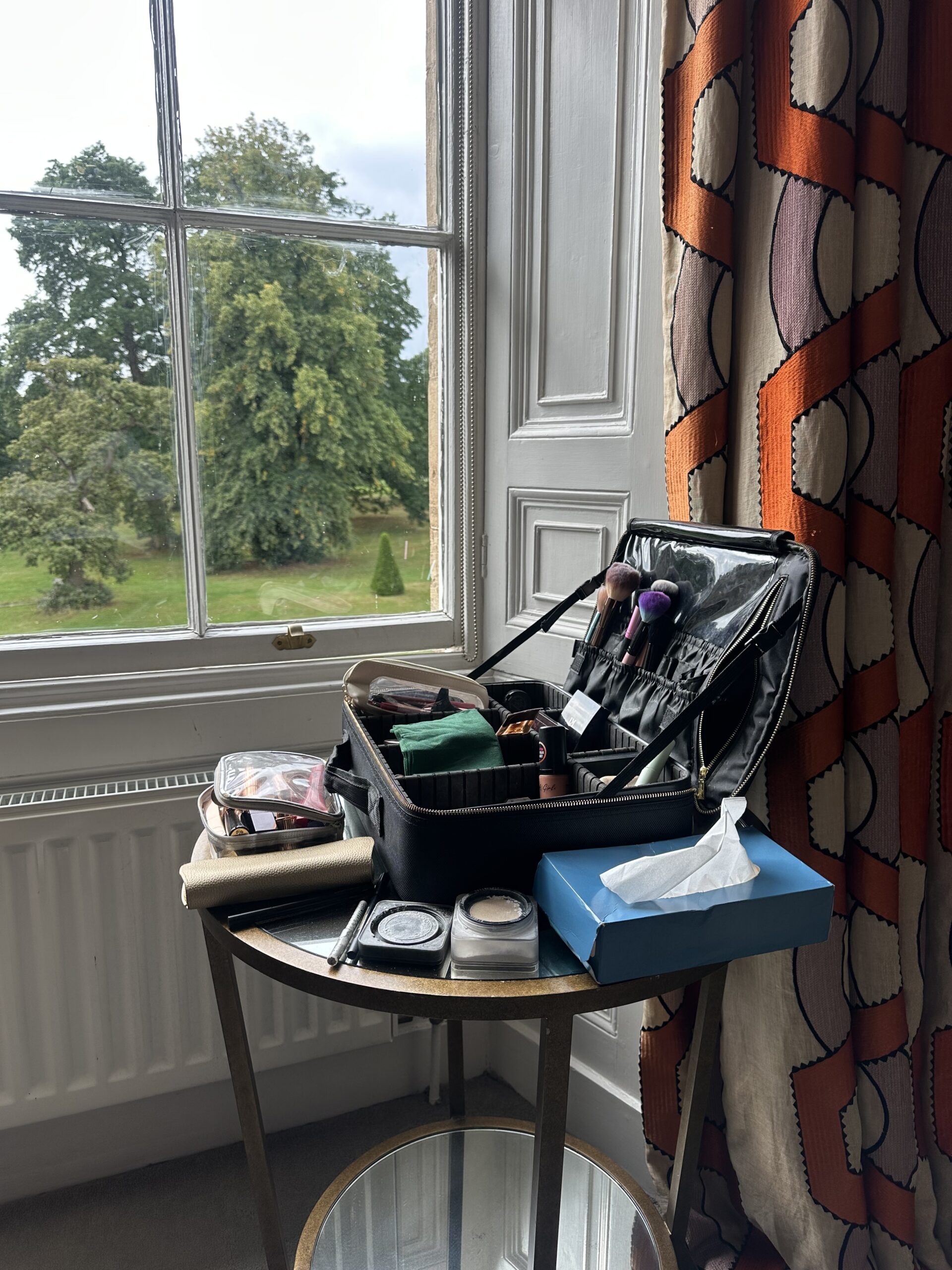 Mel’s makeup kit arranged on a table beside a window at a wedding venue